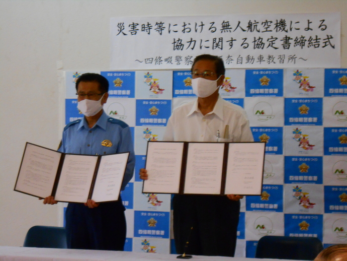 災害時等における無人航空機による協力に関する協定書締結式で男性2名が締結書を持ちながら記念撮影をしている写真