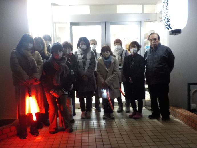 白を基調とした建物の前で手に赤いライトを持った方や反射ベストを着ている夜間パトロールに参加した方々の集合写真