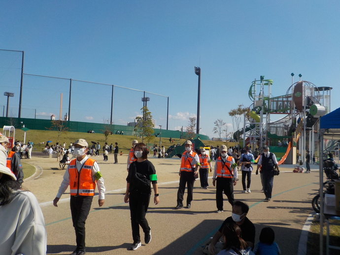堺市原池公園で、オレンジ色のベストを着た方々と関係者の方々が周りの様子を見ながら歩いている写真