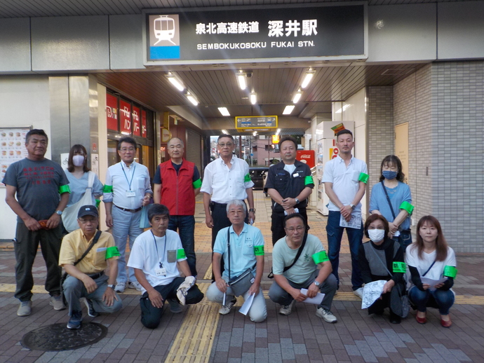 泉北高速鉄道深井駅の前で左腕に緑の腕章を付け前列の方はしゃがみ、後列の方は立っている集合写真
