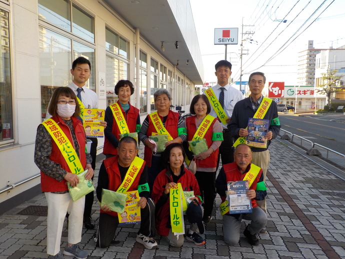 西友堺福田店の前で、赤いベストを着た方々と関係者の方々がチラシやひったくり防止カバーを持っている集合写真
