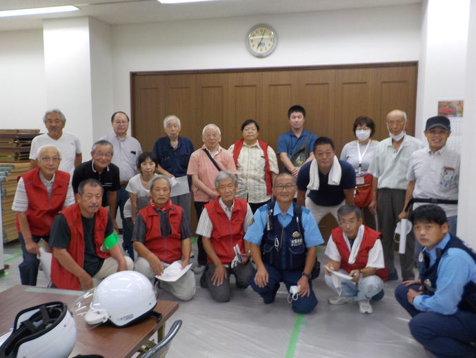 壁に時計が設置された室内で、西陶器校区自治連合会の方々と警察官の方々が前列はしゃがみ、後列は立っている集合写真