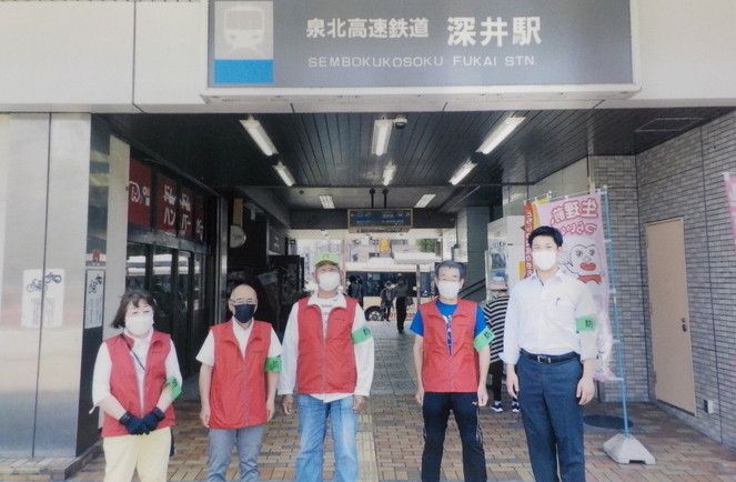 泉北高速鉄道深井駅の前で、左腕に緑の腕章を付けた1人の女性と4人の男性が立っている集合写真