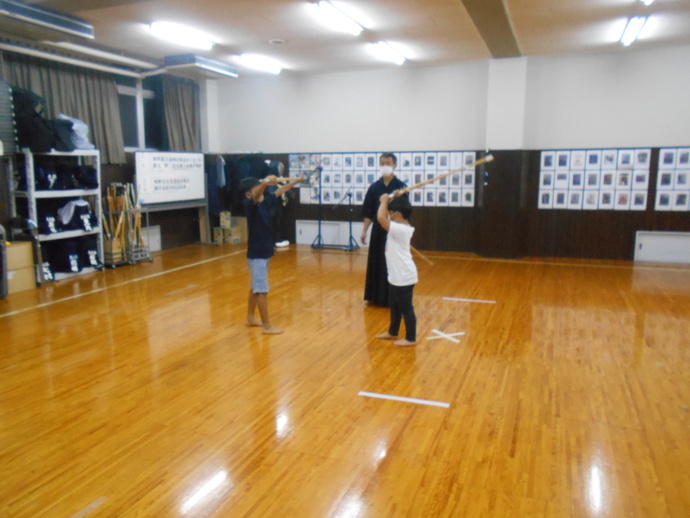 剣道着を来た師範の前で男の子2人が竹刀を持ち、剣道を練習している写真