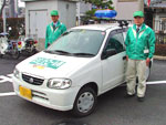 青色回転灯を装備した白い軽自動車の両脇に緑のジャンバーと帽子を被った熊取町安全パトロール隊が立っている写真