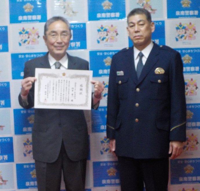 警察官の隣で賞状を見せながら記念撮影をしている読売センター和泉砂川の人の写真