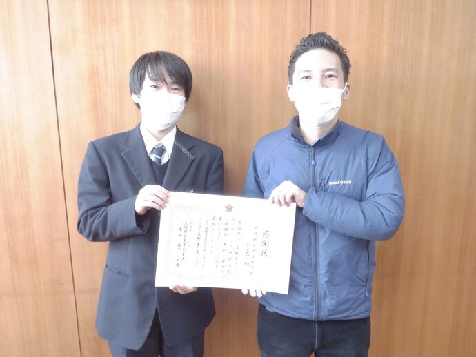 先生と高校生ボランティアの生徒が1枚の感謝状を持ちながら記念撮影をしている写真