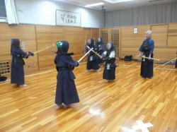 防具を着て2人1組で剣道の練習をしている2組の子供とそれを見ている指導者の写真