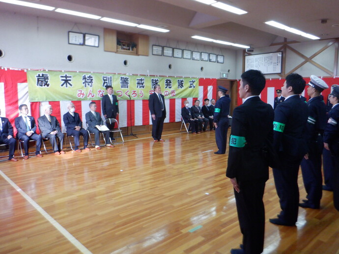 「歳末特別警戒隊発隊式」と書かかれた横断幕と紅白幕の前で椅子に腰かけている来賓の方々と向かい合って立っている警察官の写真