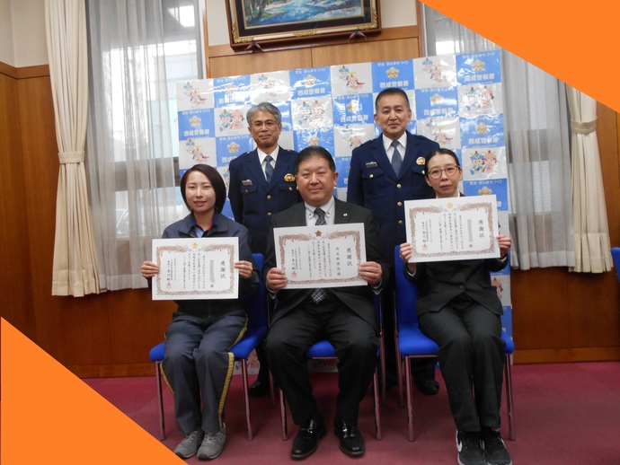 感謝状をもって椅子に腰かけている西成郵便局の3名の局員とその後ろに立っている2名の警察署員の記念写真