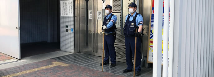 西成警察署正面玄関前に立ち、警棒を持って警備をしている2人の男性警察官の写真