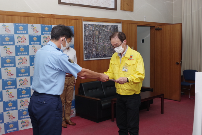 西成警察署のバックボードの前で警察の方が川田昌二さんへ感謝状を手渡している写真