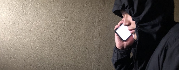 黒のフードをかぶりスマートフォンで電話をしている人の写真