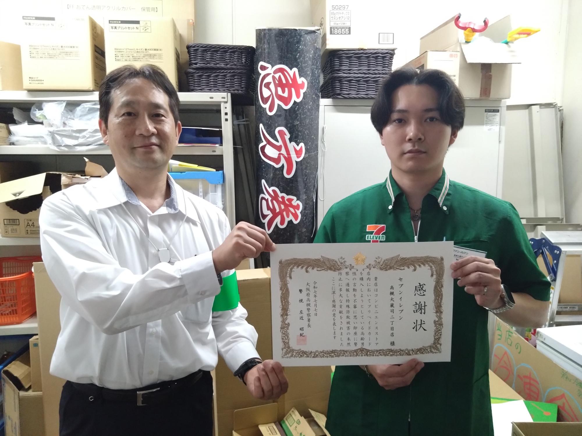 セブンイレブン大蔵司2丁目店の店員と緑色の腕章をつけた男性が一緒に感謝状を持っている写真