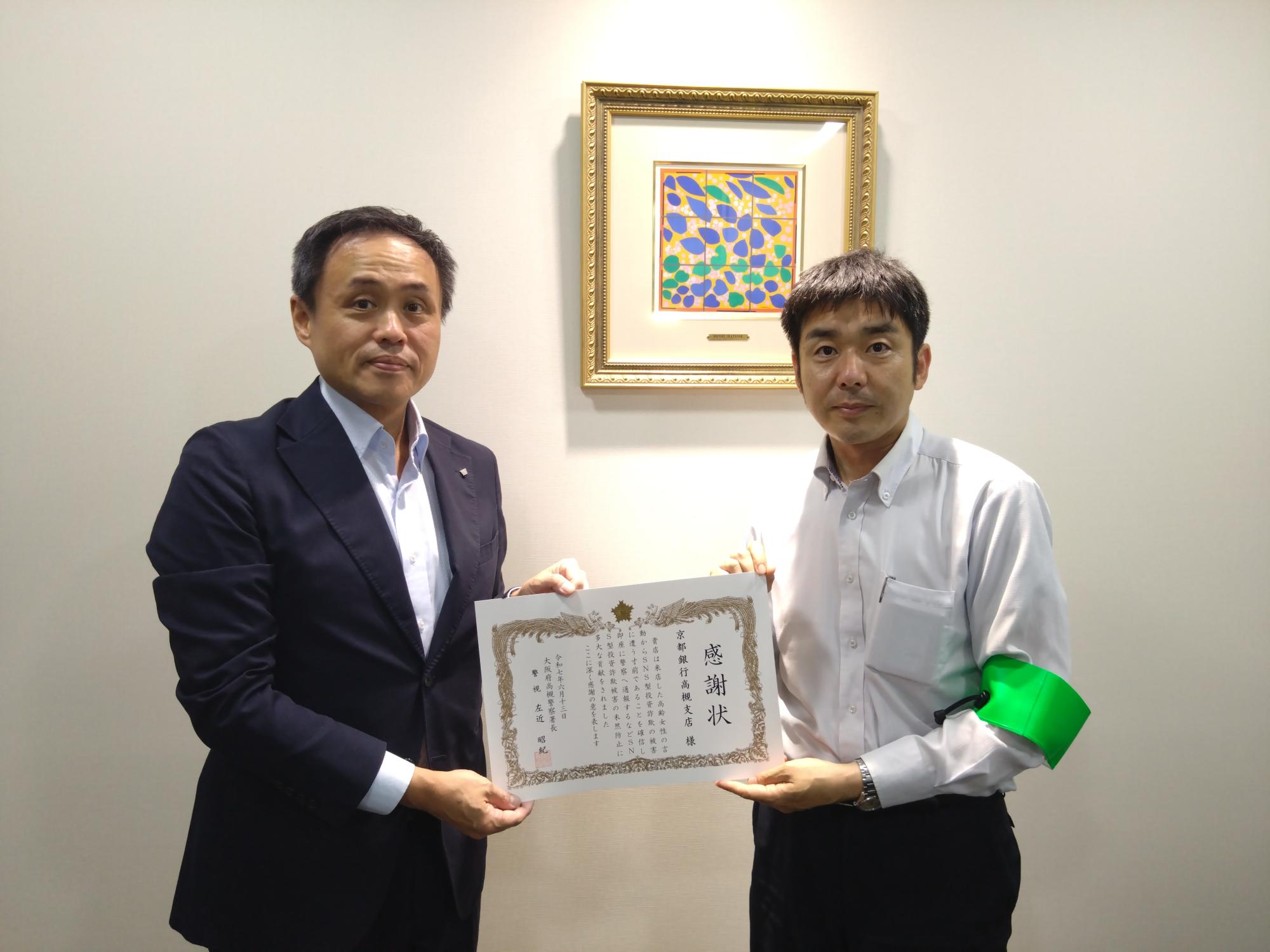 男性が感謝状を手に持ち、緑色の腕章をつけた男性と横1列に並んでいる写真