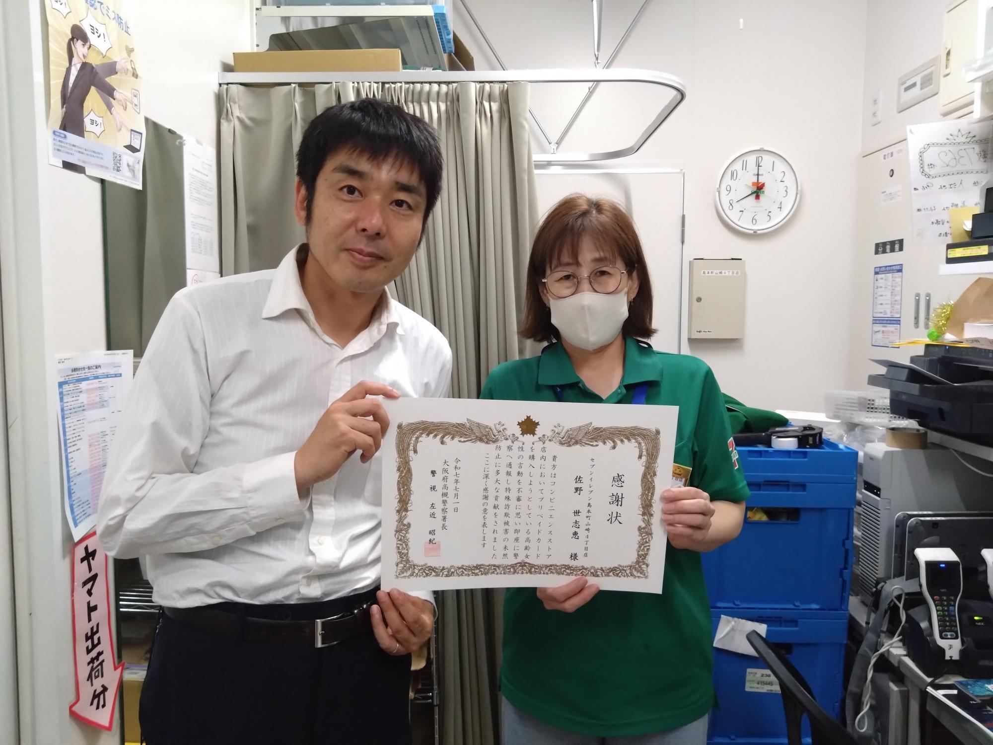 セブンイレブン島本町山崎4丁目店の店員が感謝状を手に持ち、男性と横1列に並んでいる写真