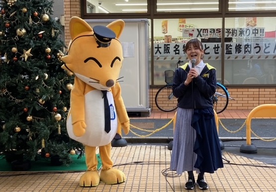 クリスマスツリーが飾られた瓢箪山ジンジャモール商店街で、瓢箪山ジンジャモールマスコットキャラクターのひょこたんと防犯ソングを披露して頂いている若林美樹さんの写真