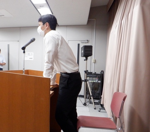 演題に手をつき話をしている男性を横から写した写真