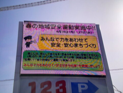パチンコ店の電光掲示板に、警察官がスピーカを持って話しているイラストと春の地域安全運動実施中!!、みんなで力をあわせて安全・安心まちづくりと表示されている広告の写真