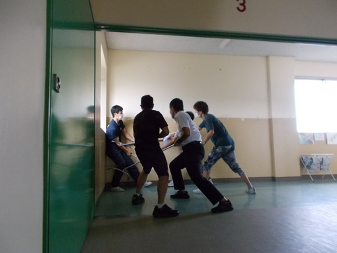 4名の男性がさすまたを使い不審者を校舎の角に追い詰めた不審者対応訓練の様子を写した写真