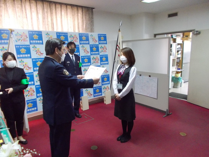 JA布忍支店の女性職員と向かい合って立ち感謝状を読み上げている警察官の写真