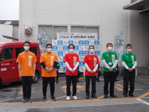 左側の2名がオレンジ色、真ん中の2名が赤色、右側の2名が緑色のTシャツを着て並んでいる写真
