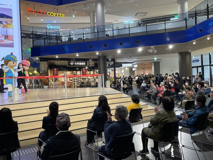 セブンパーク天美のイベント会場に大阪府警のキャラクターフーくん、ケイちゃん、マイクを持った女性が登場し、イベント会場には椅子が並べられ、たくさんの人が座って舞台を見て拍手している写真