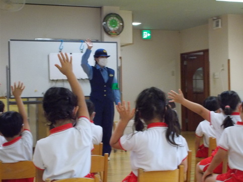 園児の前の女性警察官が右手を挙げ、園児達も手を挙げている写真
