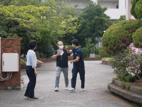 校門前で3名の職員がメモなどをみながら話し合いをしている様子の写真