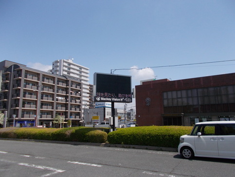 春の地域安全運動に関する広報映像が映し出された河内天美駅の電光掲示板マッキービジョンを車の通る大通りから写した写真