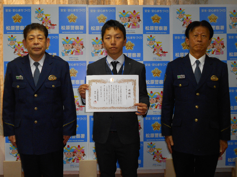 中央に感謝状を持ったセコム株式会社松原営業所の職員の男性、その両端に警察署員が並んでいる記念写真
