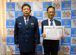 感謝状を持ったりそな銀行河内松原支店天美出張所の職員の男性と警察署員が並んでいる記念写真