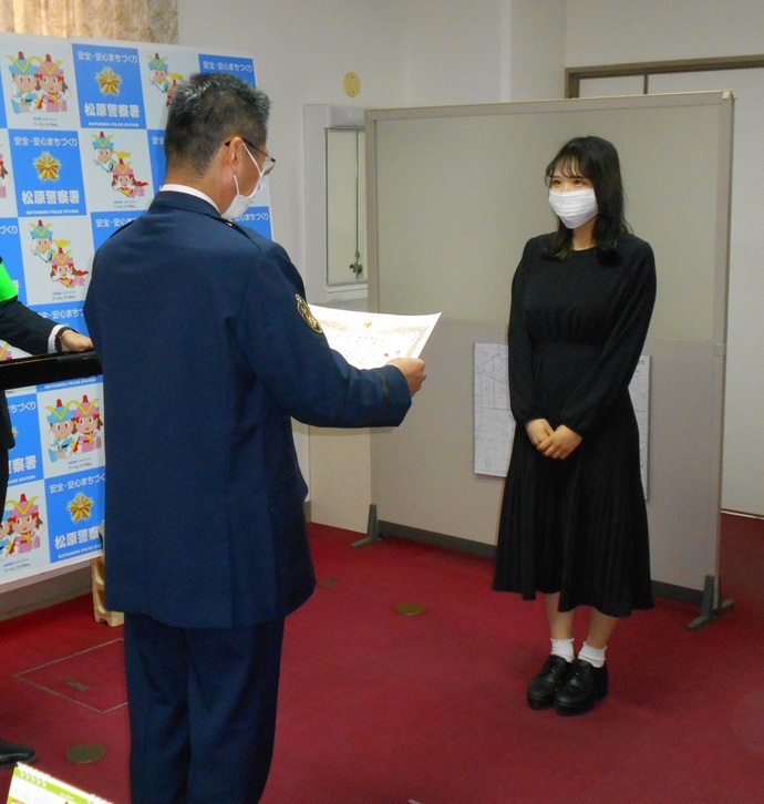 感謝状を読み上げている警察署員と向かい合って立っているベルランド看護助産大学校の学生さんの写真