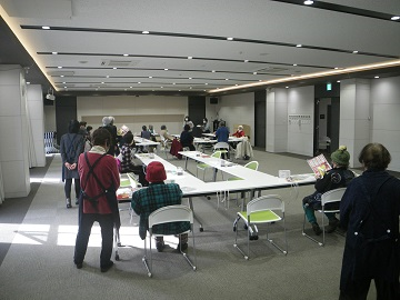 高齢者参加のハンドメイド教室で松原警察署オリジナル特殊詐欺被害防止啓発チラシと安全安心まちづくりしんちゃんラムネを配布後、前の方で2人の方が話している写真
