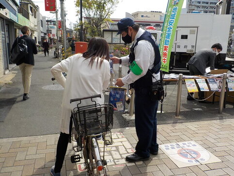 自転車に乗ってる女性に、警察官が特殊詐欺被害防止の啓発品の配布している写真