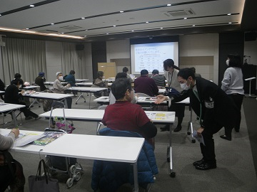 シニア向けスマートフォン教室に訪れている男性に、安まちアプリ登録を説明している写真
