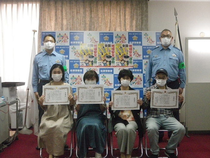特殊詐欺を未然に防いだ4人が感謝状を手に持ち椅子に座り、その後ろ両端に警察官が立って記念撮影している写真