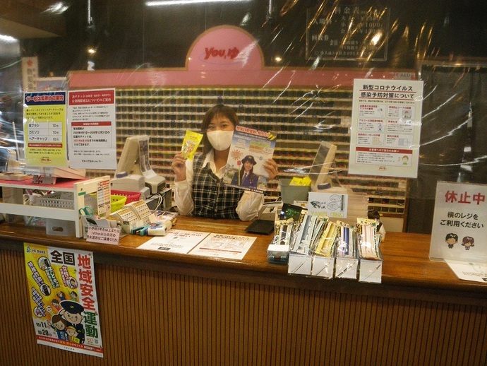 天然温泉you,ゆ~のフロントの女性従業員が特殊詐欺被害防止のチラシを両手に持っている写真