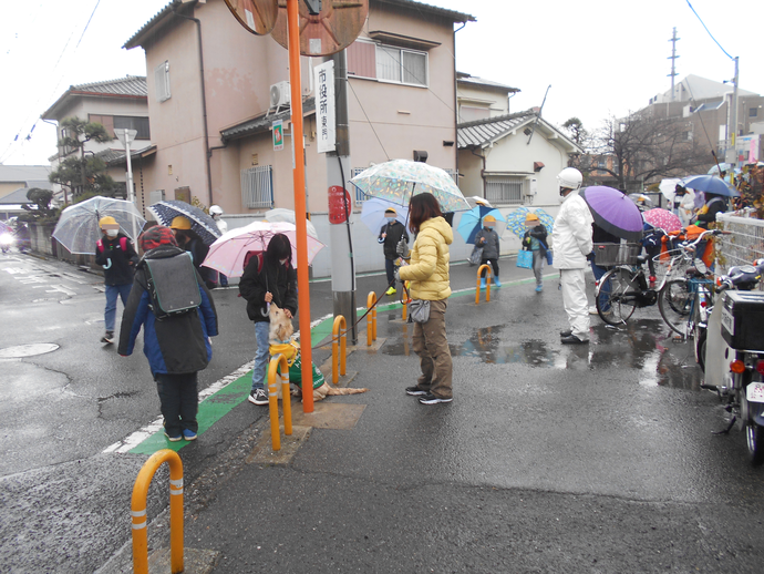 傘を持ち下校している複数の児童を警察官と松原わんわんパトロール隊・ボランティアの方が見守り、女の子が犬の頭を撫でている写真