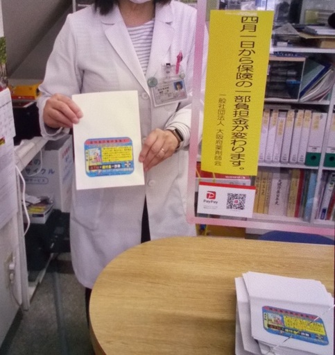 特殊詐欺被害防止啓発のイラストが書かれた封筒を持って立っている薬剤師の写真