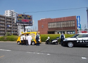 「NPO法人やんちゃまファミリーwith」の黄色の車の前で、4名の女性と男性警察官が立っている写真