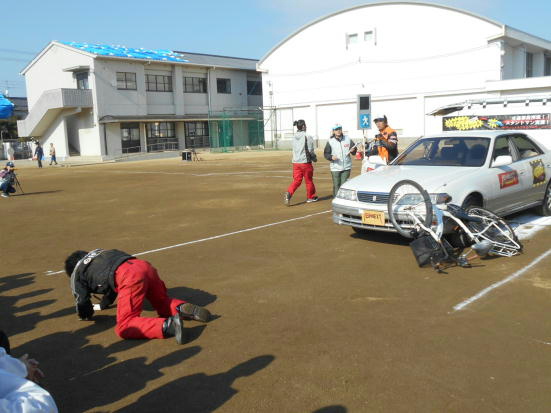 車の左側のヘッドライト付近に自転車が倒れ、自転車に乗っていた人が5メートルほど飛ばされて道路にうずくまっている写真
