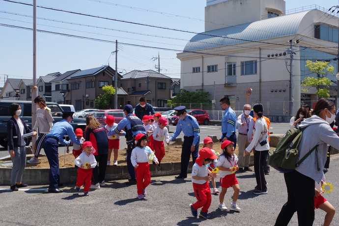先生や制服警察官に手を借りながら花壇から下りている園児たちの写真