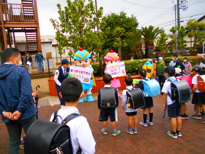 婦人警官、大阪府警察マスコット「フーくんとケイちゃん」が話してるのを、ランドセルを背負った子供たちが見ている写真