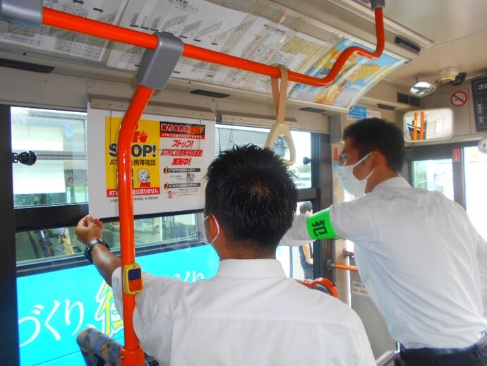 バスの車内に広告を取り付ける男性二人の写真