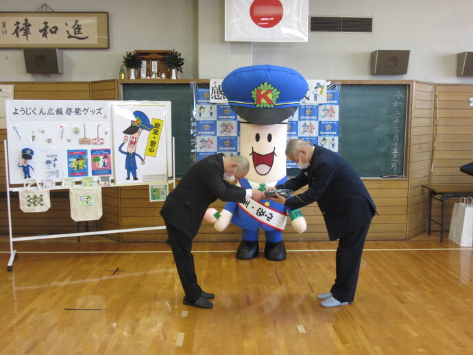 ようじくんが見守る中、河内長野事業場防犯協会の関係者が河内長野警察署長から記念品を贈呈されお互いに頭を下げている様子の写真