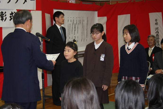優秀賞者の子どもたちが並び、先頭の女の子が河内長野警察署長から賞状を授与される様子の写真