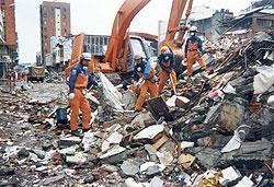 瓦礫が山積した状況で活動をしている国際緊急援助隊の写真（後方には重機がある）