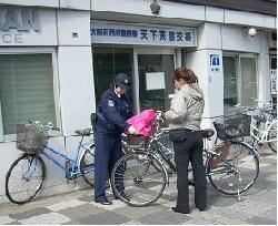 天下茶屋交番の前で女性の自転車にひったくり防止カバーの取り付けをしている様子