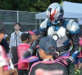 大阪のご当地ヒーロー「地球戦士ゼロス」がが来場した子どもたちにうちわを手渡している様子
